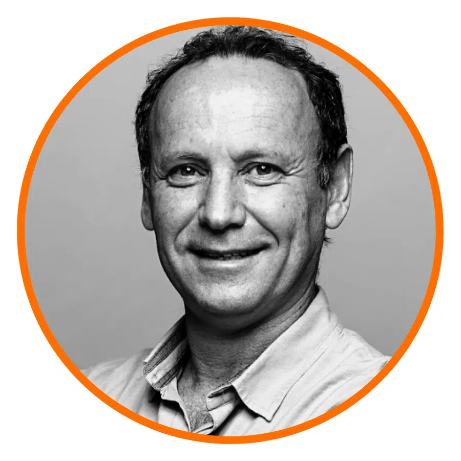 Smiling man with short hair in a button-up shirt, shown in a black and white photo with an orange circular border.